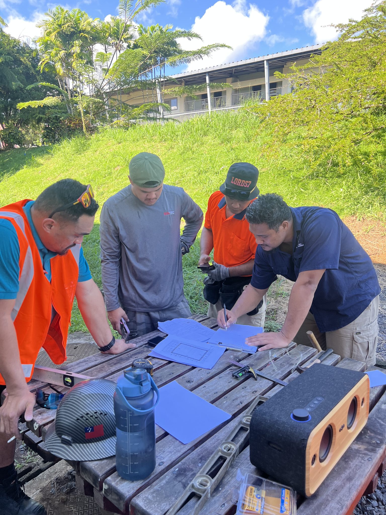 Participants reviewing plans and marking timber at an outdoor workbench.